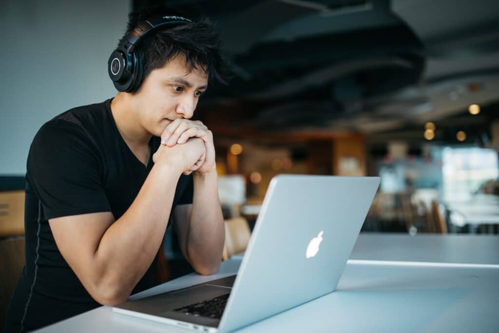 un estudiante adulto que usa audífonos mira atentamente la pantalla de su computadora portátil.
