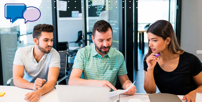 Tres colaboradores discutiendo documentos en una reunión de trabajo en equipo.