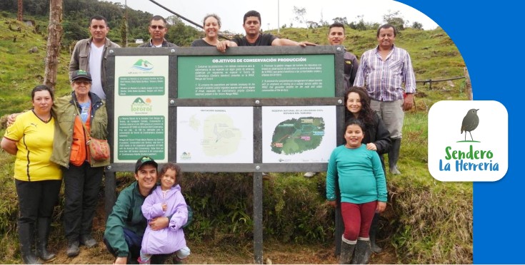 Sendero La Herrería family standing by a conservation sign in Guayabetal, Colombia, highlighting community and environmental impact.
