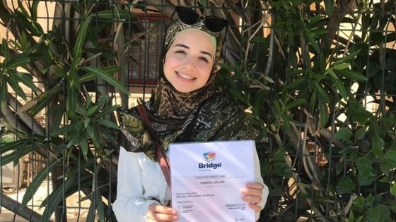 a female teacher holding up her Bridge TEFL certificate and smiling.