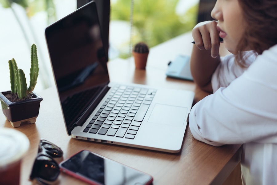 an online student sitting at a desk, looking at her laptop screen.