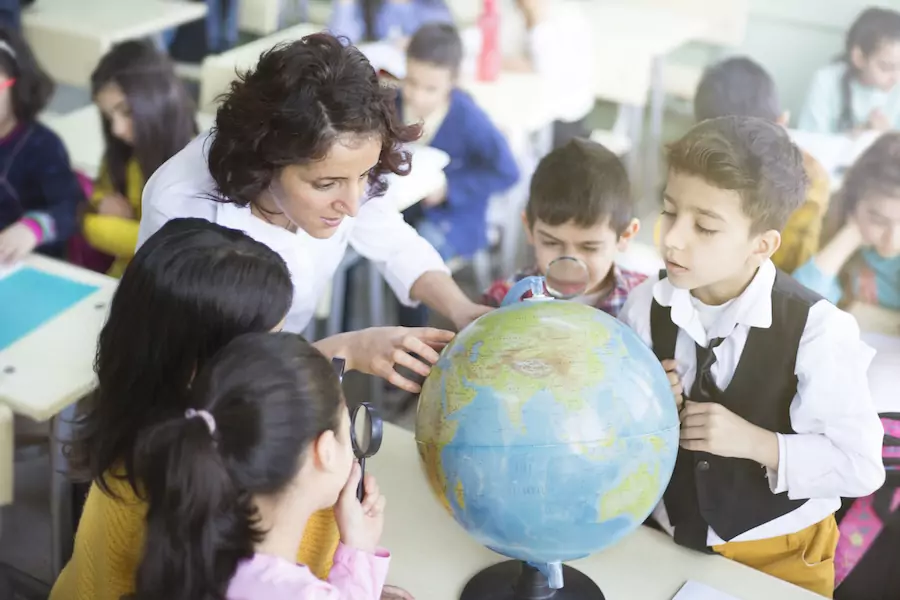 a female teacher and her young students gathered around a world globe as she points to a location.