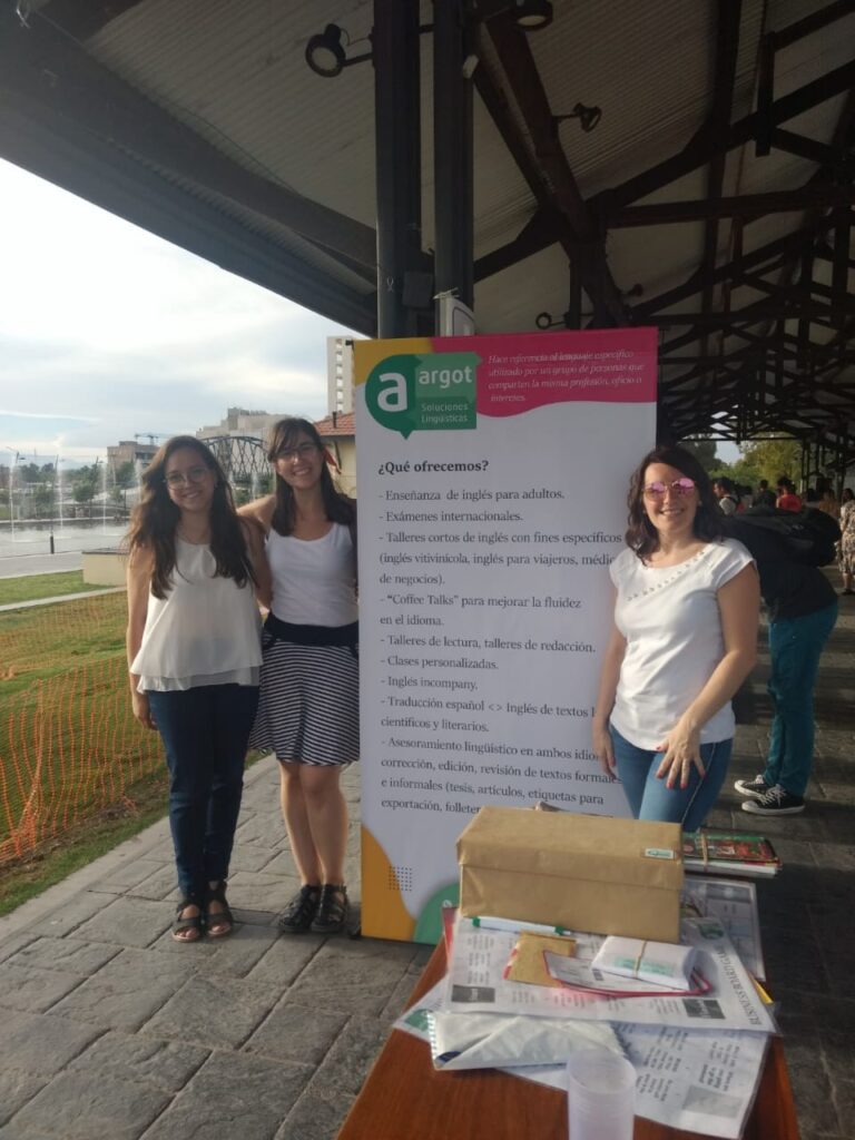 Josefina, her business partner, and a teacher pose next to a banner for her teaching institute. 