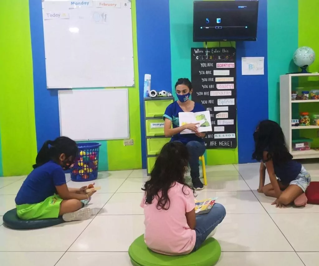 An ESL teacher sitting on the floor and reading to young learners.