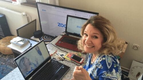 A smiling teacher gives the thumbs up while using digital teaching tools on her computer
