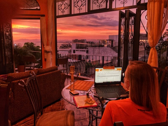 Rachel working on her laptop looking out the window at a sunset in Puerto Vallarta.