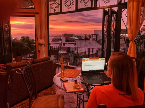 Rachel working on her laptop looking out the window at a sunset in Puerto Vallarta.