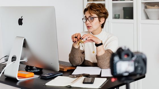 a female teacher looks at her computer monitor while sitting at a desk covered in notes.