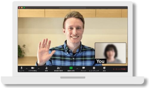 A smiling ESL teacher waves to his online student over his laptop.