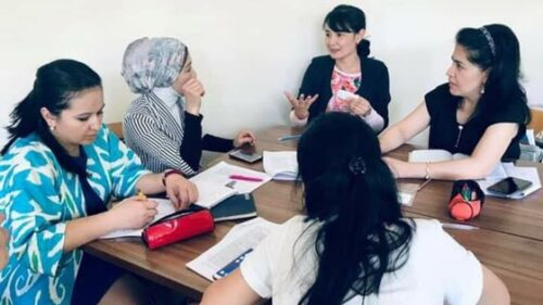 Adult students and their teacher sitting at a table having a conversation.