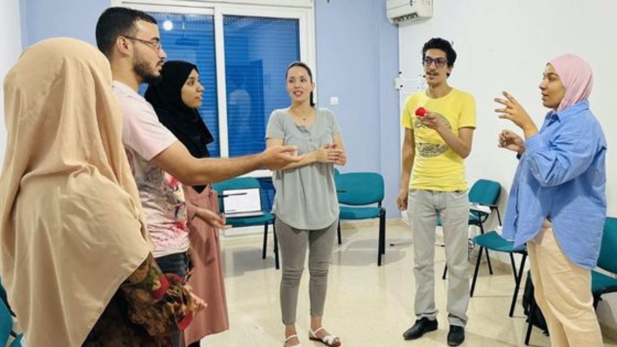 An image of an English teacher standing in a circle with a group of ESL students practicing suprasegmentals