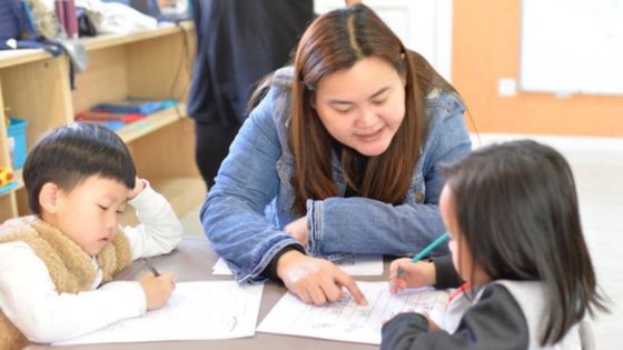 An English teacher works with two young learners on a worksheet