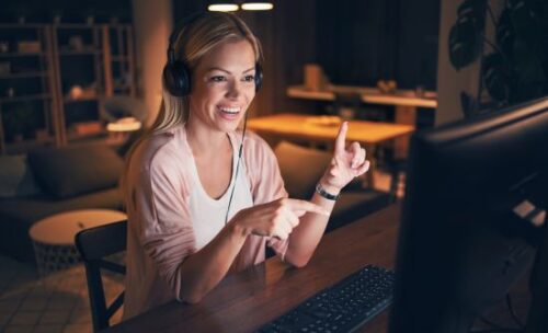 female teacher gestures to her laptop screen as she teaches an online student.