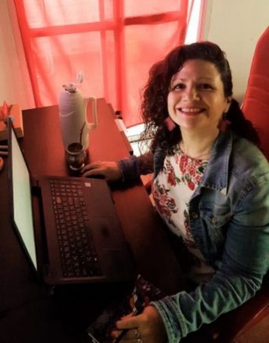 Andrea smiling at the camera, sitting at her desk in front of her laptop.