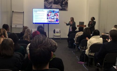 Bridge's Director of Operations, Anna Hearrell points to a projector as she discusses integrating culture into instruction before a room full of IATEFL audience members.