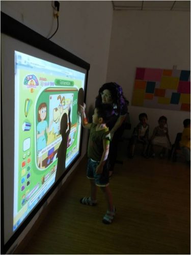 Andrea teaching ESL to a young boy using a large projector. 