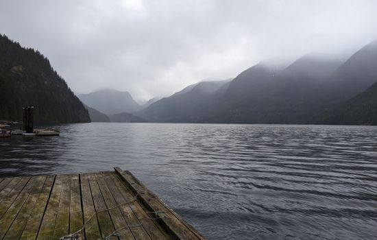 a lake view off a doc with fog covered mountains in the background.