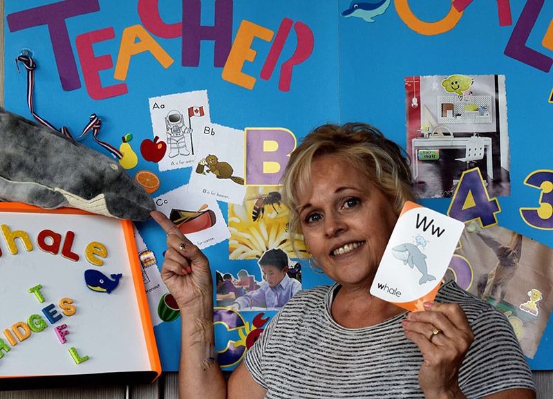 An image of an English teacher using ESL lesson plans while holding a flashcard for the letter W and pointing to a stuffed whale.