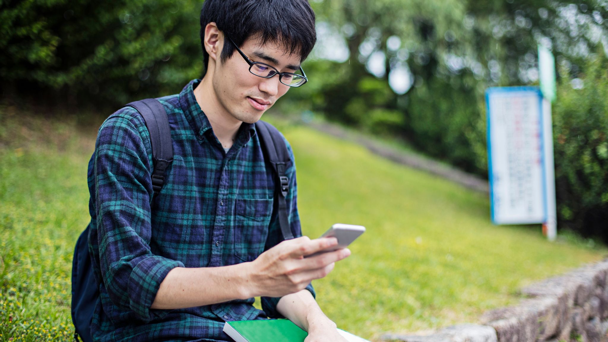 a young adult student sitting on campus looking at his smartphone.