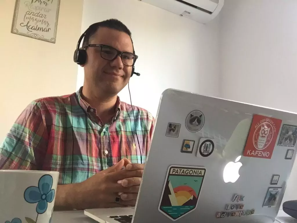 an online ESL teacher smiles at his students onscreen. 