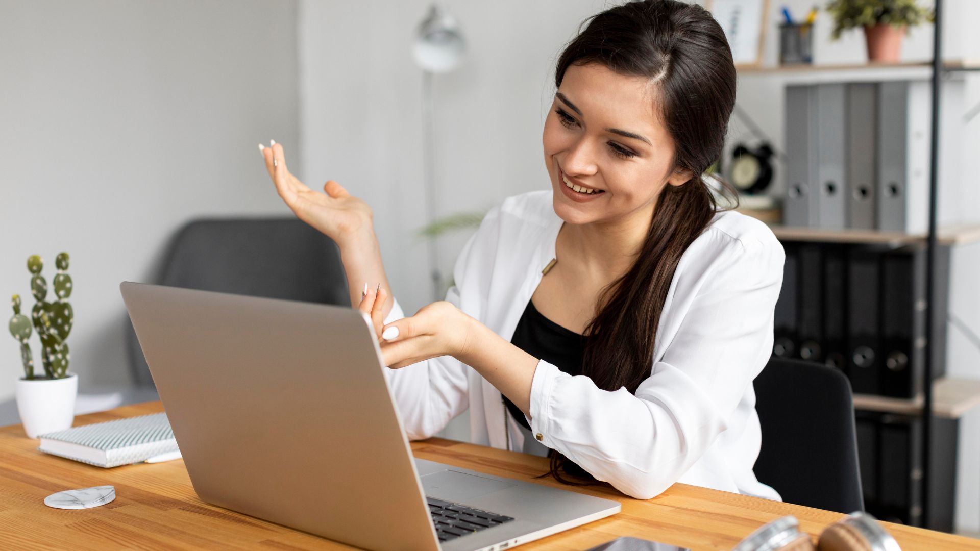 a woman smiling and gesturing at her laptop