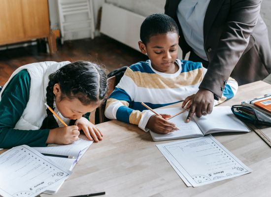 a teacher leans over a boy working on a workbook assignment