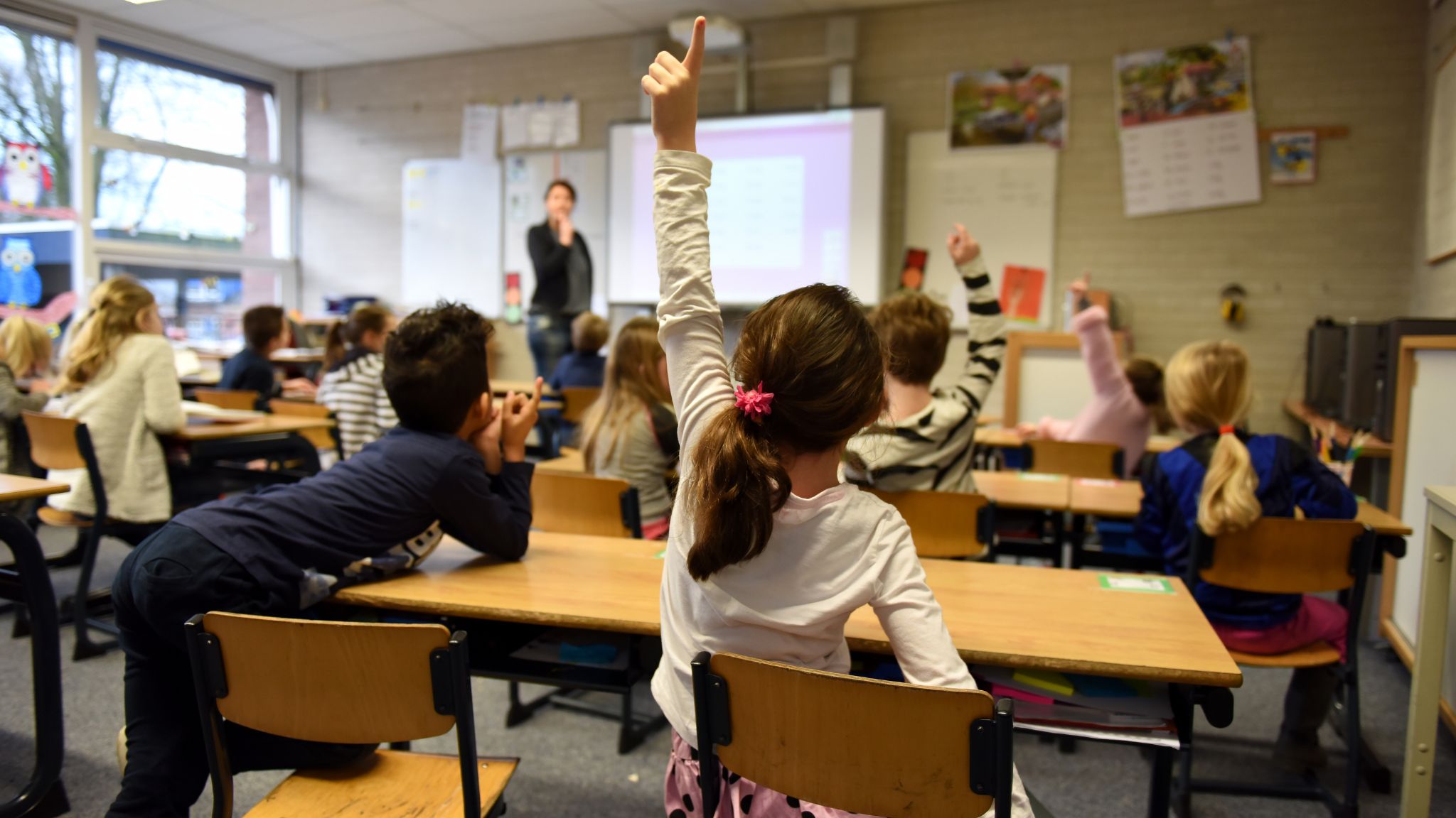 a student in the back of the classroom raising her hand high