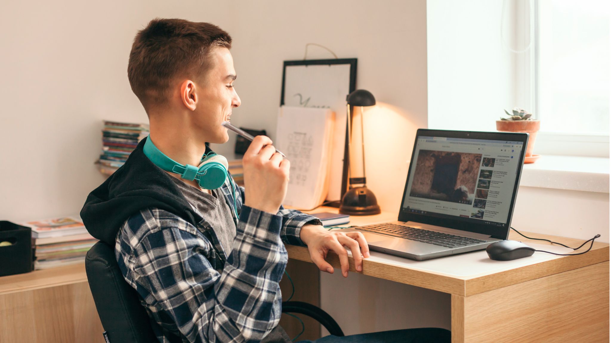 Teenaged learner watches videos on his laptop at his desk.