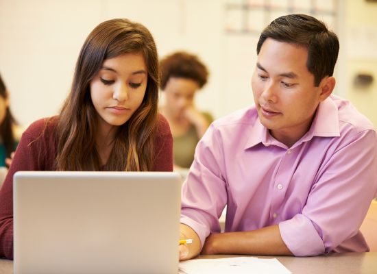 a teacher and student looking at a laptop during class