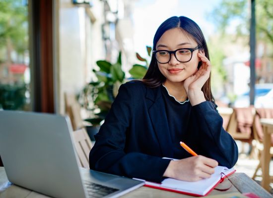 a woman looking at her laptop while taking notes