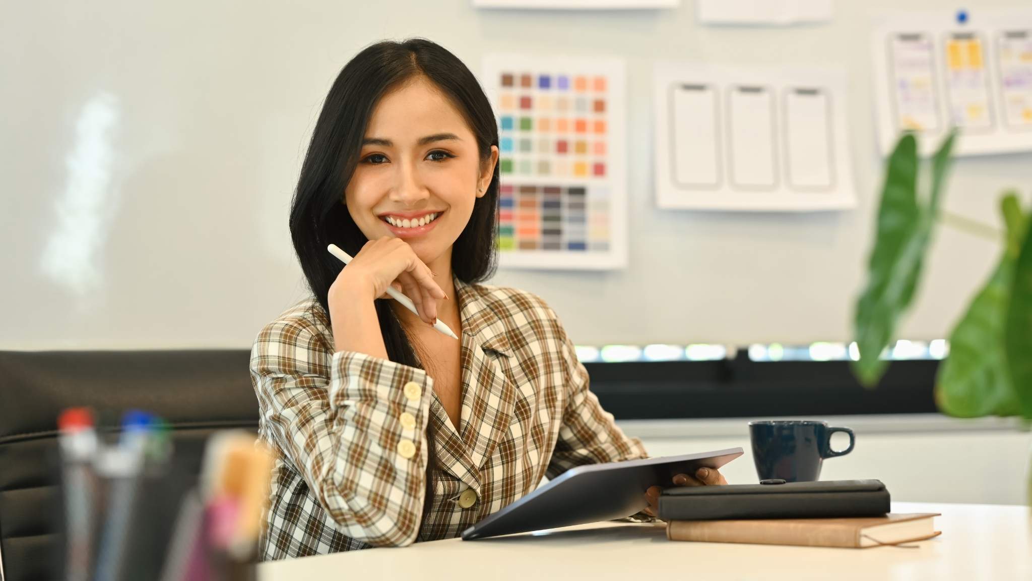 An image of a female teacher sitting at a desk taking notes on a tablet