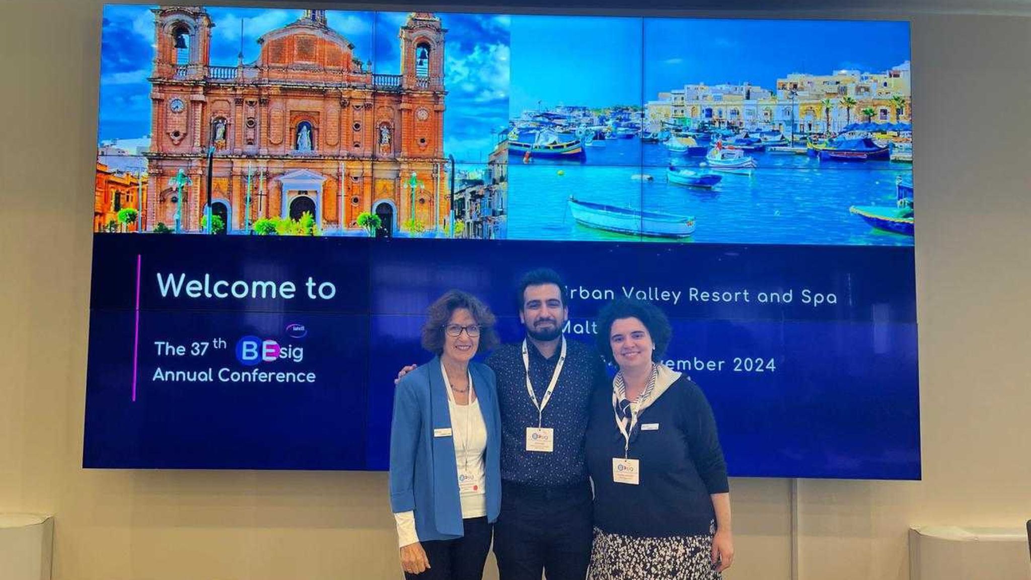 An image of Umut and two other people standing in front of the screen welcoming people to the IATEFL BESIG conference