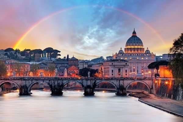 An image of Rome, Italy with a rainbow going over a bridge and the river. 