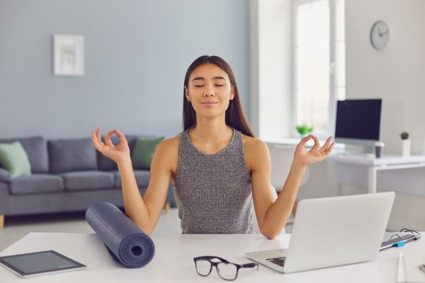 An image of a woman sitting at a desk in a meditation pose