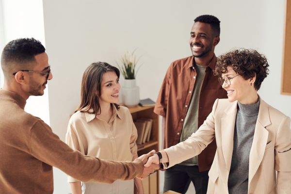 An image of four business professionals from diverse backgrounds, shaking hands and smiling