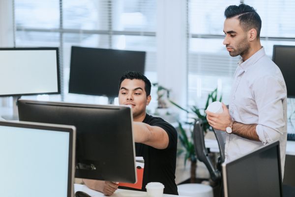 Una imagen de dos personas mirando una pantalla de computadora en una oficina.