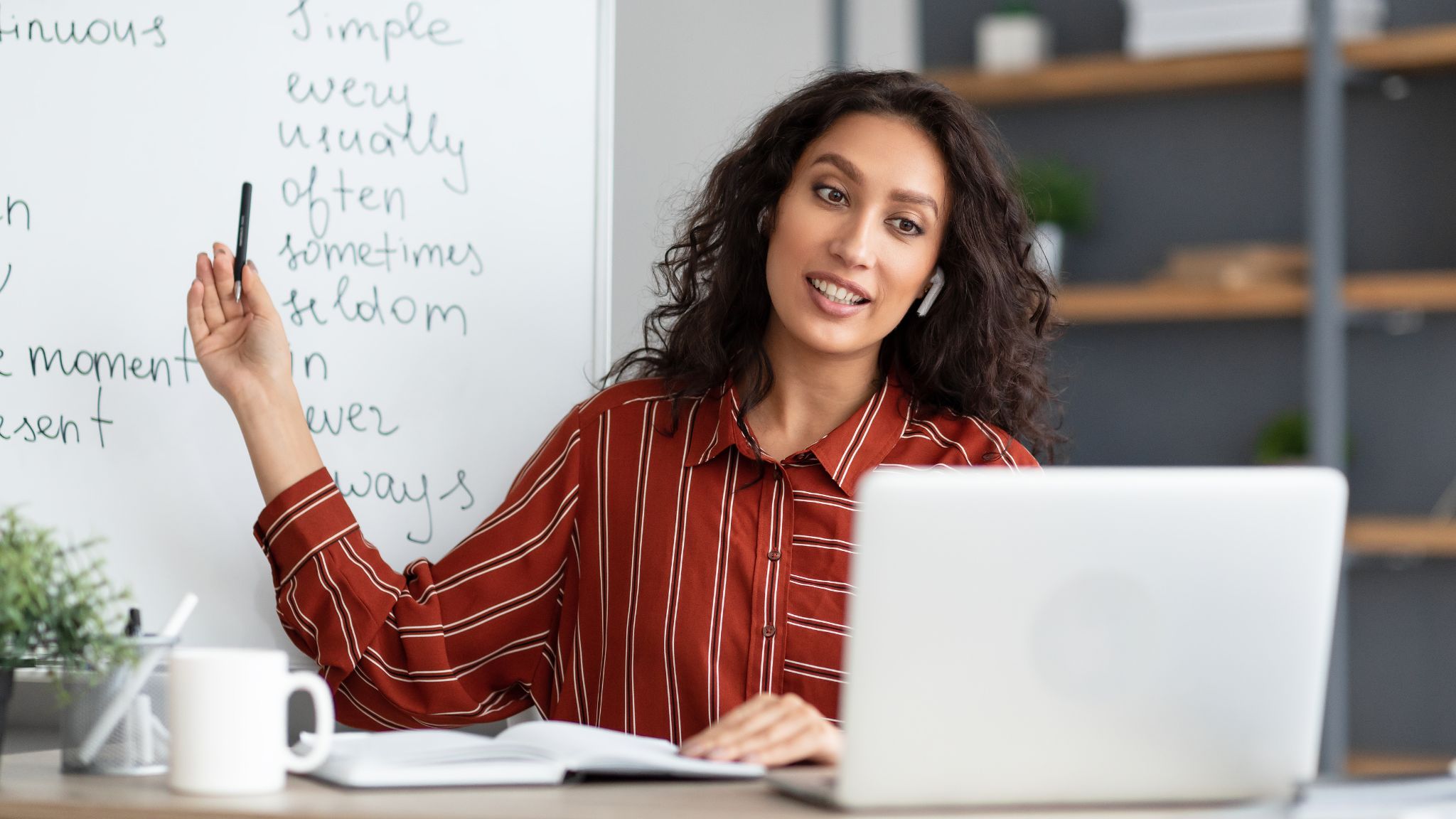 An image of a teacher sitting at a desk, pointing to a whiteboard while teaching English online