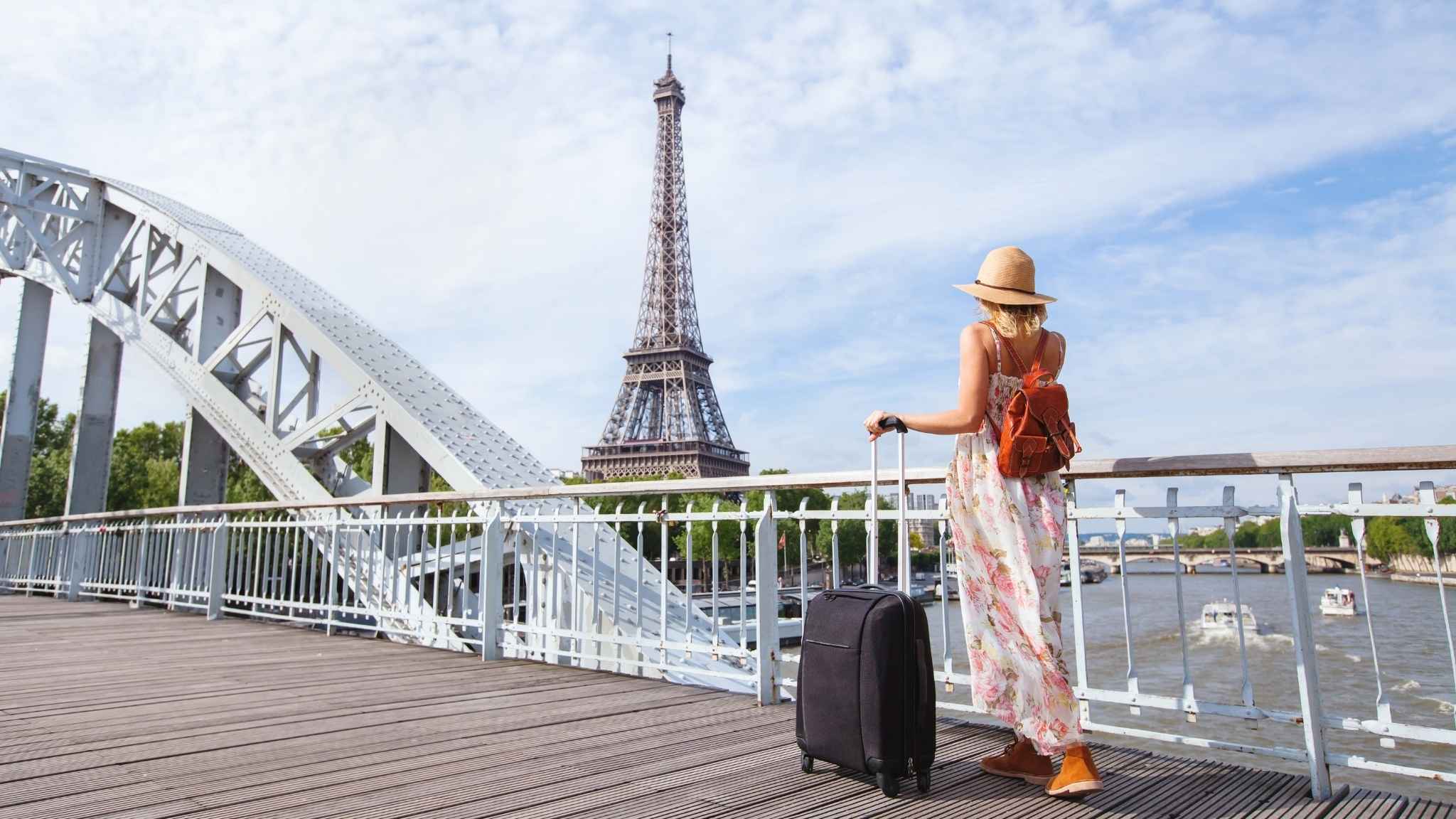 An image of a person standing on a bridge with a suitcase looking at the Eiffel Tower