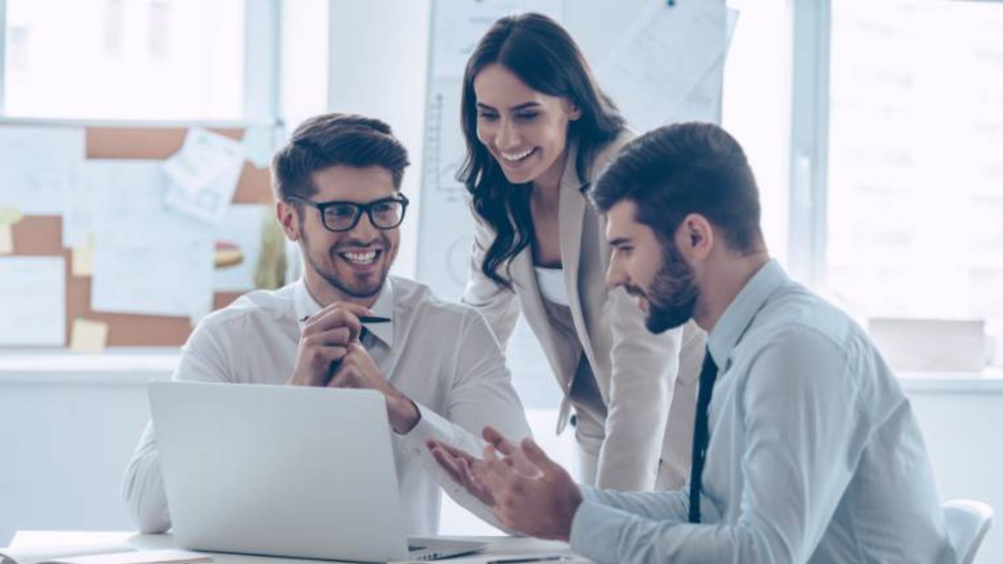 An image of 3 coworkers looking at a laptop and having a business english conversation