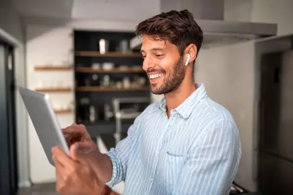 An image of a smiling man using an English speaking app on his tablet