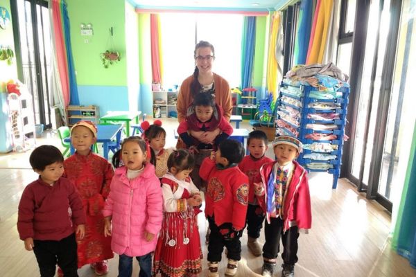 An image of a Bridge TEFL graduate smiling, standing in her classroom with her English students in China