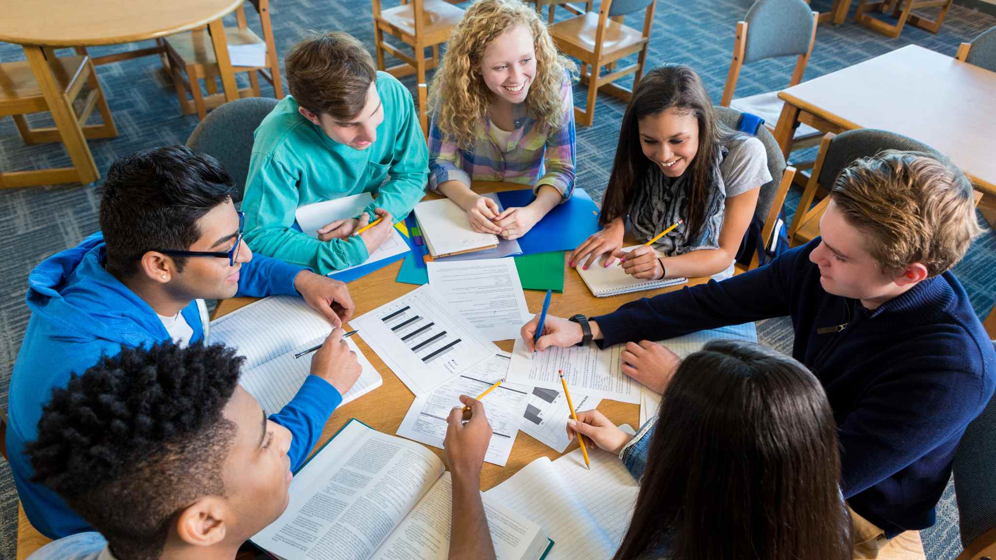 An image of a group of teenagers sitting around a table with their English teacher