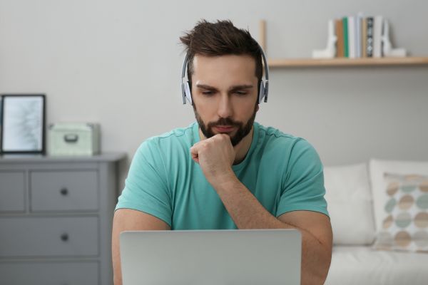 An image of a man wearing headphones and looking intently at a laptop