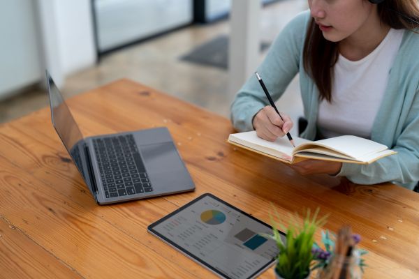 An image of an ESL student sitting at a desk with a laptop and tablet, taking notes