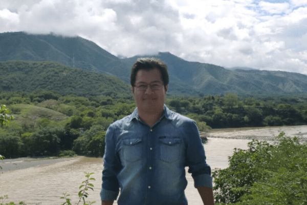An image of a male English teacher with a river and mountains in the background
