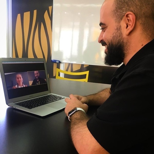 A man participates in an online video meeting on his laptop, smiling as he interacts with a student on screen during a virtual English class.