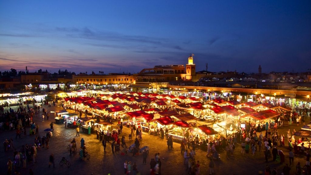 Night view of Marrakech’s Jemaa el-Fnaa market filled with people and glowing food stalls.