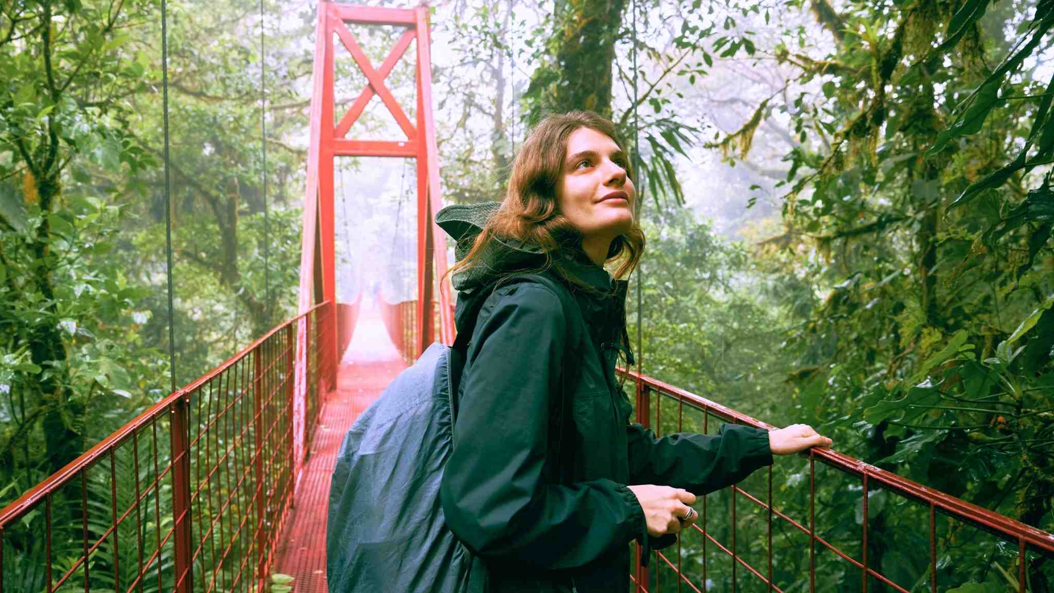 Traveler walking on a red hanging bridge through the rainforest in Monteverde, Costa Rica, symbolizing the adventure and natural beauty you can experience when you teach English in Costa Rica.