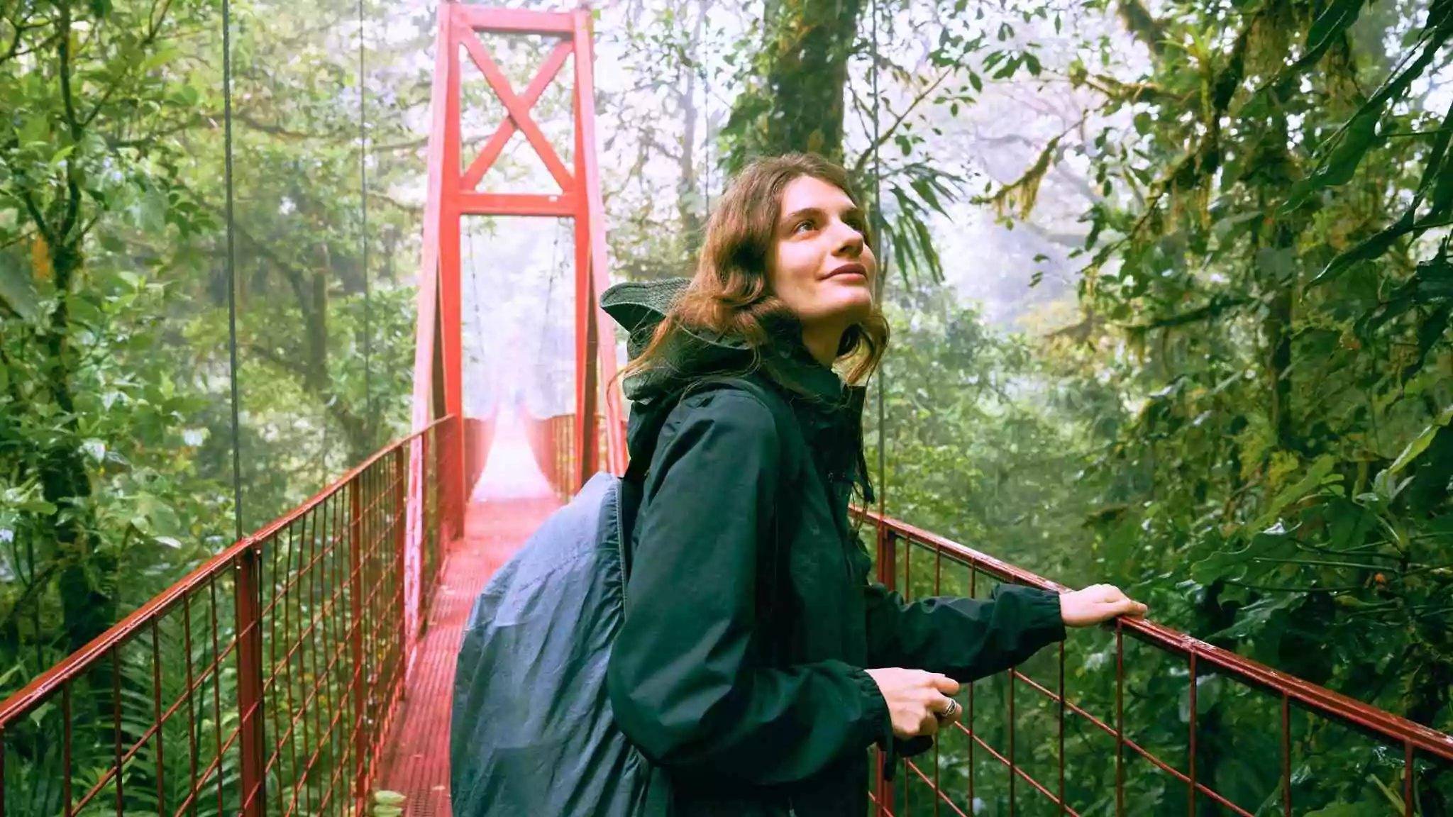 Traveler walking on a red hanging bridge through the rainforest in Monteverde, Costa Rica, symbolizing the adventure and natural beauty you can experience when you teach English in Costa Rica.