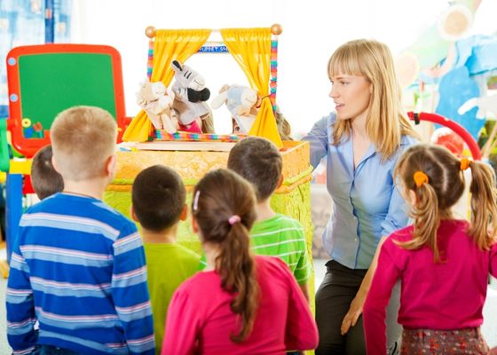 A teacher uses puppets to perform a skit with young learners.